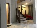 Spacious living room with marble flooring, modern chandelier, and wooden staircase