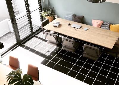 Modern dining room with large wooden table, four chairs, pendant lights, and a mix of decorative pillows on sofa with access to balcony.