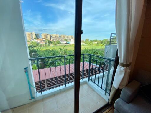 View of a balcony with railing, overlooking a green landscape and buildings in the distance