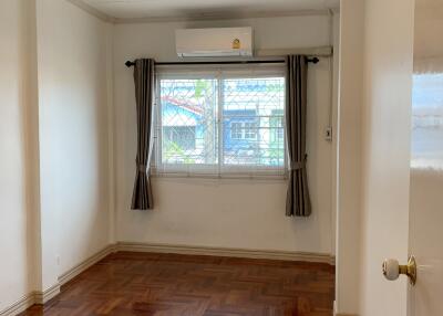 Bedroom with wooden parquet floor, window with curtains, and air conditioning unit