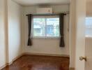 Bedroom with wooden parquet floor, window with curtains, and air conditioning unit