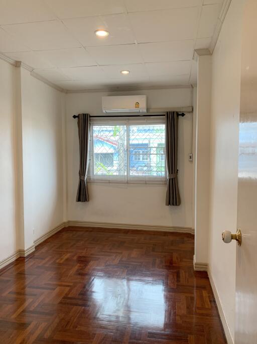 Bedroom with wooden parquet floor, window with curtains, and air conditioning unit