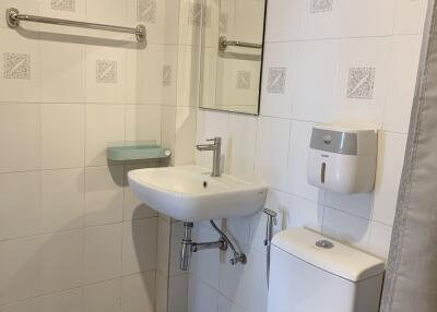 Small, white-tiled bathroom with sink, toilet, mirror, and towel rack