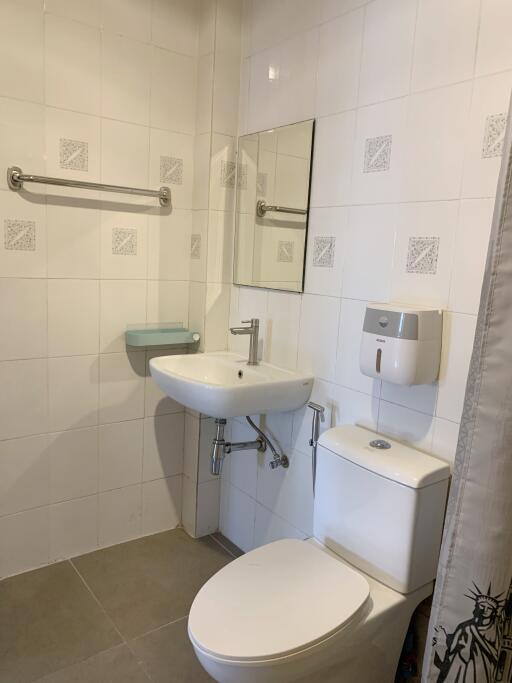 Small, white-tiled bathroom with sink, toilet, mirror, and towel rack