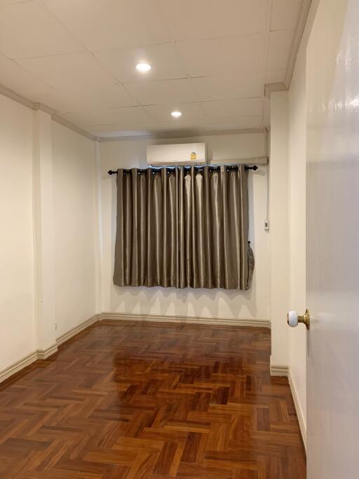 Empty bedroom with wooden flooring, ceiling lights, and curtains