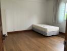 Spacious unfurnished bedroom with single mattress and hardwood floor.