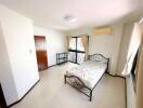 Spacious bedroom with ample natural light, featuring a metal frame bed and white tiled floor.