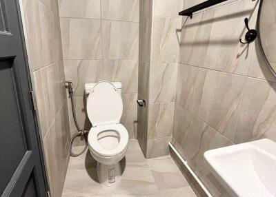 Modern bathroom with tiled walls and floor, featuring a toilet, wall-mounted sink, and a round mirror