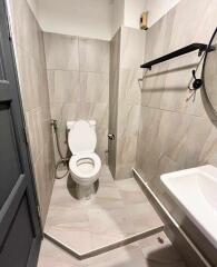 Modern bathroom with tiled walls and floor, featuring a toilet, wall-mounted sink, and a round mirror