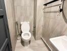 Modern bathroom with tiled walls and floor, featuring a toilet, wall-mounted sink, and a round mirror