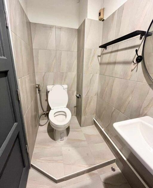 Modern bathroom with tiled walls and floor, featuring a toilet, wall-mounted sink, and a round mirror