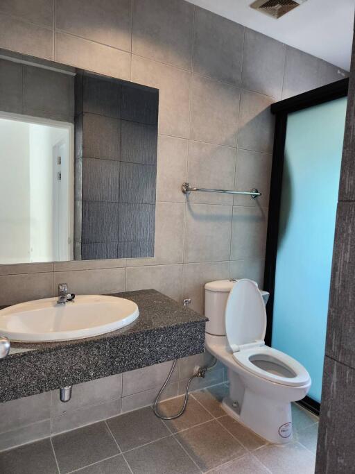 Modern bathroom with tiled walls, a sink with a large mirror, and a toilet