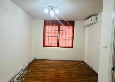 Empty room with wooden floor, windows with red blinds, and ceiling light.