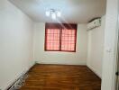 Empty room with wooden floor, windows with red blinds, and ceiling light.