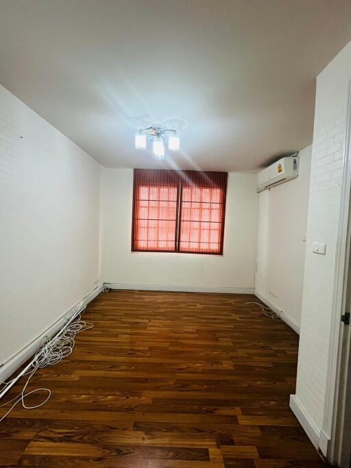 Empty room with wooden floor, windows with red blinds, and ceiling light.