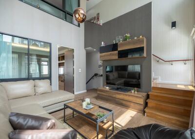 Modern living room with large windows, beige sofas, wooden furnishings, and a flat-screen TV