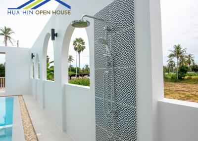 Outdoor shower area with patterned tile wall next to a pool