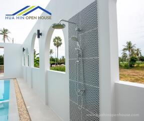 Outdoor shower area with patterned tile wall next to a pool