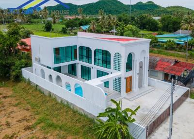 Two-story white building with large windows, arches, and a pool