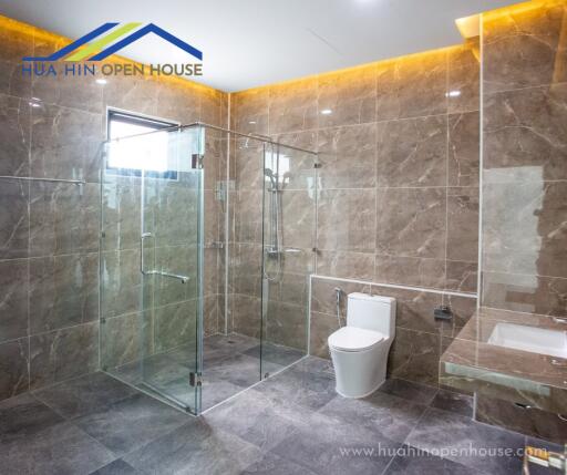 Spacious modern bathroom with glass shower enclosure and stone tile walls