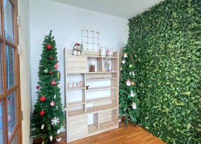 Room with green leafy accent wall, two Christmas trees, and a wooden shelf