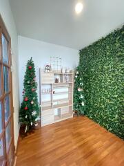 Room with green leafy accent wall, two Christmas trees, and a wooden shelf