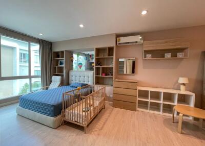 Spacious bedroom with large window, bed, baby crib, storage units, and air conditioning