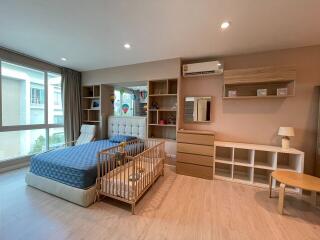 Spacious bedroom with large window, bed, baby crib, storage units, and air conditioning