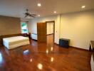 Spacious bedroom with wooden flooring, bed, ceiling fan, and ample natural lighting