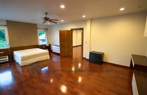 Spacious bedroom with wooden flooring, bed, ceiling fan, and ample natural lighting