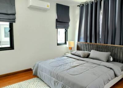 Modern bedroom with large bed, windows with dark curtains, and a wall-mounted air conditioner