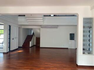 Spacious living area with wooden flooring, visible stairs, and large windows