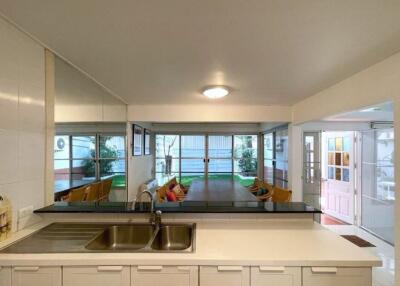 A modern kitchen with a sink, white cabinets, and view to a dining area and garden.