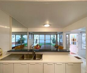 A modern kitchen with a sink, white cabinets, and view to a dining area and garden.