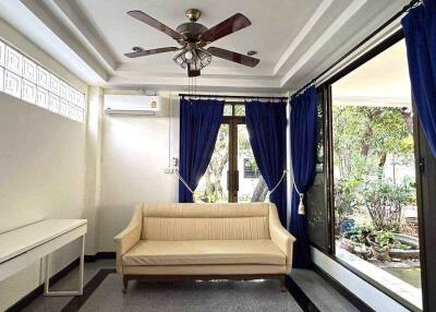 Living room with a beige couch, ceiling fan, air conditioner, and large windows with blue curtains