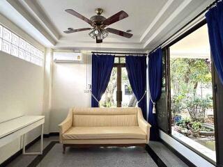 Living room with a beige couch, ceiling fan, air conditioner, and large windows with blue curtains