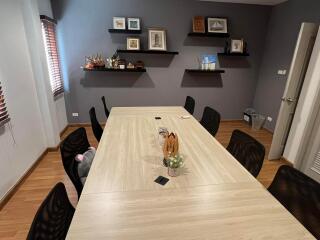 A modern meeting room with a large table and several chairs, wooden floor, and wall-mounted shelves with decor