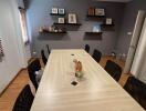 A modern meeting room with a large table and several chairs, wooden floor, and wall-mounted shelves with decor