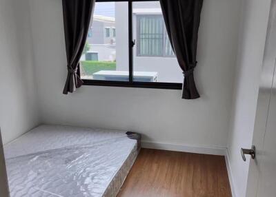 Minimalist bedroom with mattress on wooden floor, window with dark curtains, and air conditioner