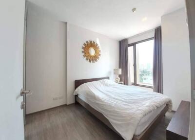 Bedroom with a large bed, wall-mounted sunburst mirror, and window with city view.