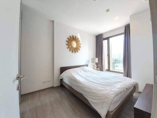 Bedroom with a large bed, wall-mounted sunburst mirror, and window with city view.