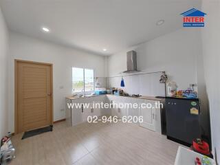 Modern kitchen with light wood door and window, white cabinets, stainless steel hood, and black refrigerator