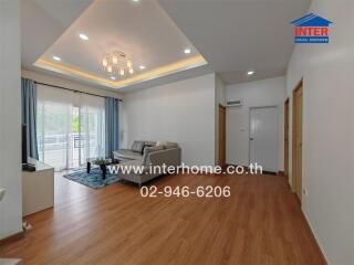 Modern living room with wooden flooring, sofa set, and sliding glass doors leading to a balcony.