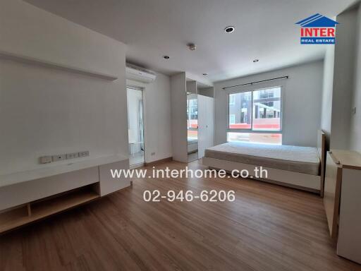 Spacious bedroom with a large window, wooden flooring, and a built-in air conditioning unit.