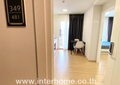 View of entrance to a room with wooden flooring, a desk and chair, and a bed in a background.