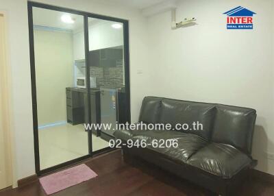 Living area with a black leather sofa and view into the kitchen