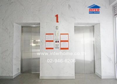 Elevator lobby in a building with two elevators and signage showing the floor number and contact details