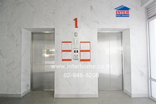 Elevator lobby in a building with two elevators and signage showing the floor number and contact details