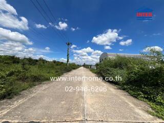 Rural road leading to a property with vegetation and a warehouse