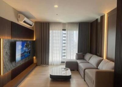 Modern living room with a sectional sofa, TV on a marble accent wall, and large window with sheer curtains